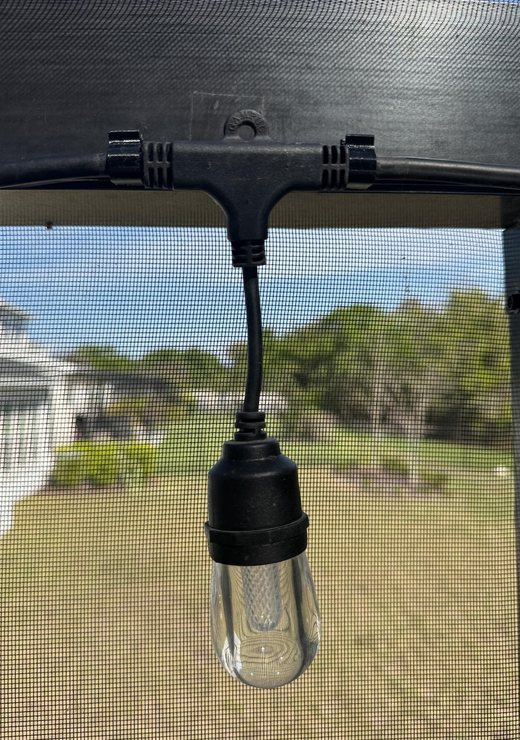 String light bulb hanging from a snap-on clip on the pool cage frame