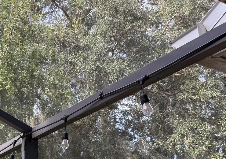 String lights running along a pool cage beam on snap-on clips in daylight