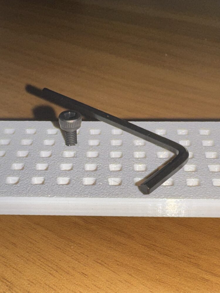 Close-up of the grid of square holes with a socket-head screw seated in one hole and the included hex key